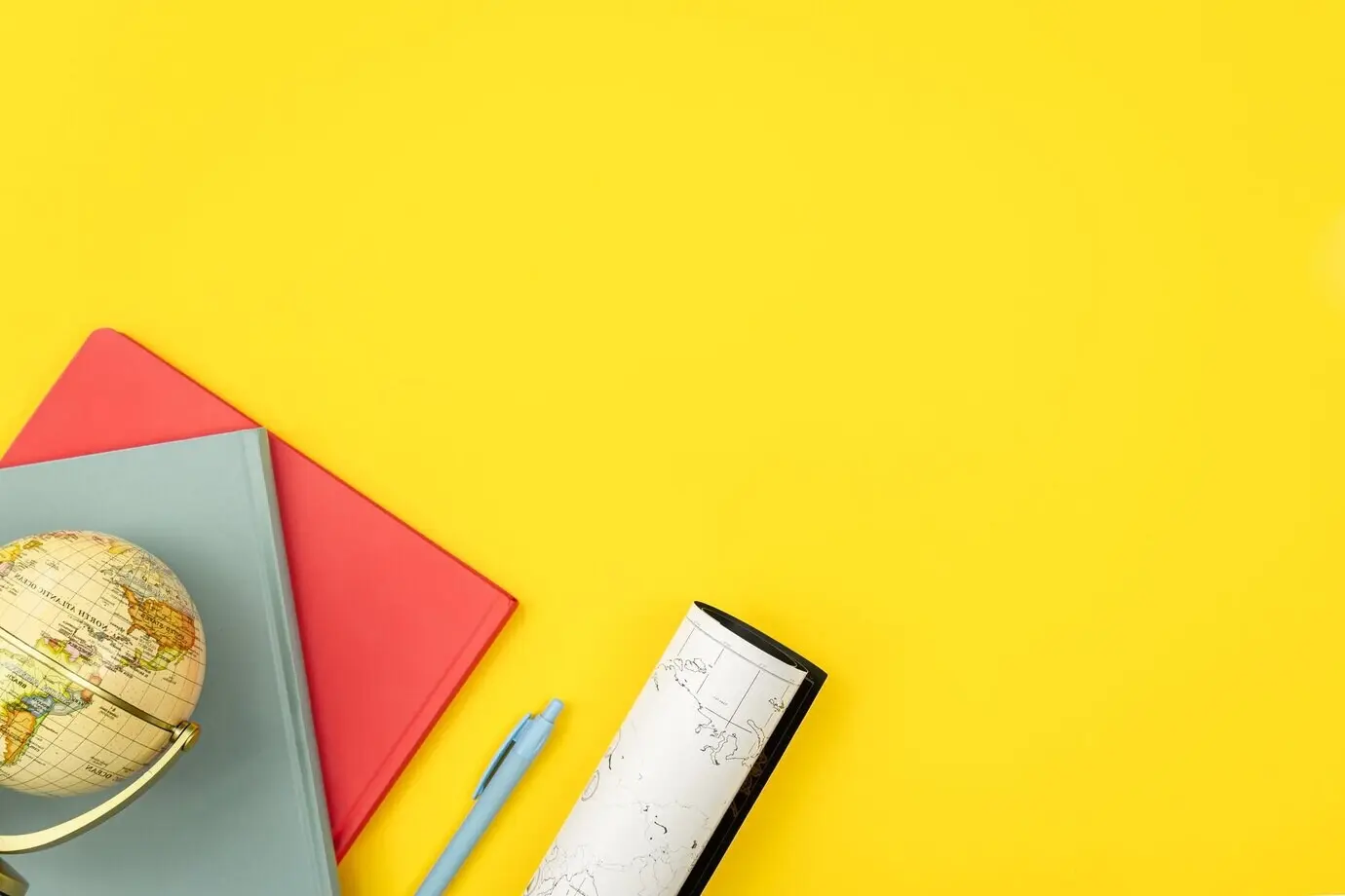 Notizbücher, Globus und Landkarte in Draufsicht auf gelbem Hintergrund.