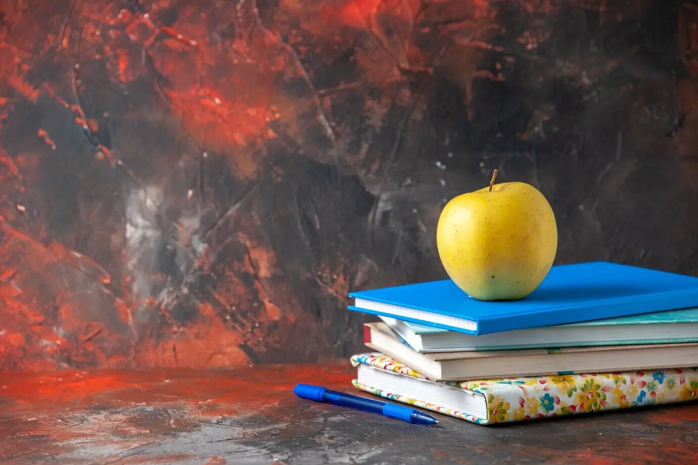 Horizontale Ansicht eines frischen gelben Apfels auf gestapelten Notizbüchern auf der linken Seite vor dunklem Hintergrund.